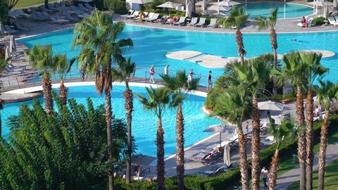 Antalya, Turkey - October 25, 2019: Aerial top view of several blue pools of hotel resort. Tourists enjoy summer vacations at beautiful green territory of luxury hotel. Real time 4k video footage.