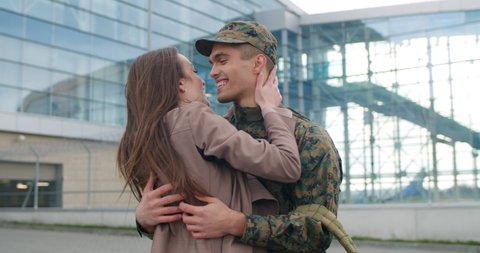 Excited soldier coming back from military service welcomed by his wife. Happy girl greeting and hugging her boyfriend in military uniform. Concept of happy reunion and military service