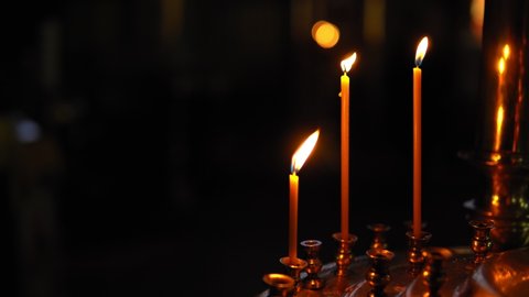 Three burning candles in a gold candlestick in Church on a dark background. Dark room of Orthodox Church lit only by wax candles. Theme religious faith and God, culture and traditions of Orthodoxy.