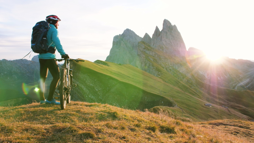 Young man with mountain bike standing on Seceda mountain peak at sunrise. Puez Odle, Trentino, Dolomites, Italy. Royalty-Free Stock Footage #1043933131