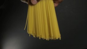 Man holds golden color raw spaghetti pasta on the dark black background