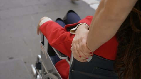 young brunette woman holding her boyfriend' s hand pushing her wheelchair
