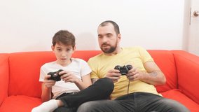 Virtual, video game. Caucasian bearded man playing video games with son indoors, sitting on sofa, holding joysticks in hands. Enjoy, leisure