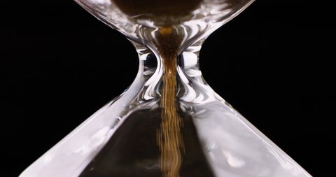 Sand moves through hourglass. Extreme close up of hour glass clock. Old time classic sandglass timer. Closeup sand is falling down and measuring time