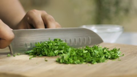 Cook hands chop coriander on a black board on a table with a large cook knife