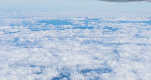 Stunning footage of aerial view above clouds from airplane window with blue sky. 