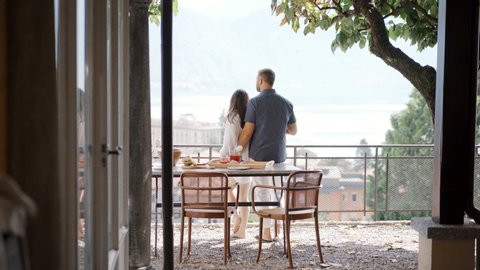 Anonymous couple enjoying breakfast on terrace
Back view of young man and woman hugging and admiring town while standing on balcony during breakfast in morning