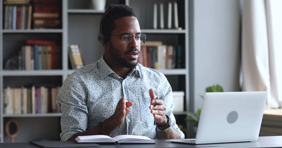 Serious young african businessman wear headset conference calling by webcam, focused mix race student study with online teacher in video chat look at laptop talk during videoconference at home office | Shutterstock HD Video #1043980210