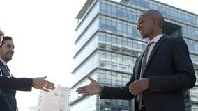 Business colleagues meeting and talking on street. Low angle view of multiethnic young business colleagues greeting each other and shaking hands on street. Business meeting concept