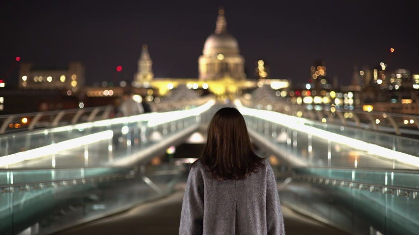 Tracking shot of a tourist young woman walking on Millennium Bridge with London St Paul Cathedral illuminated view at night Royalty-Free Stock Footage #1043988958