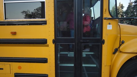 Doors of school bus opening and elementary age schoolchildren going out one by one, smiling asian female driver waving and saying them goodbye. Cute diverse preadolescent kids leaving school bus