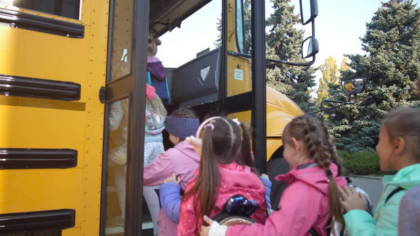 Rear view of diverse elementary age students pushing each other while getting on yellow school bus after lessons. Happy preadolescent schoolkids boarding school bus at the end of studies