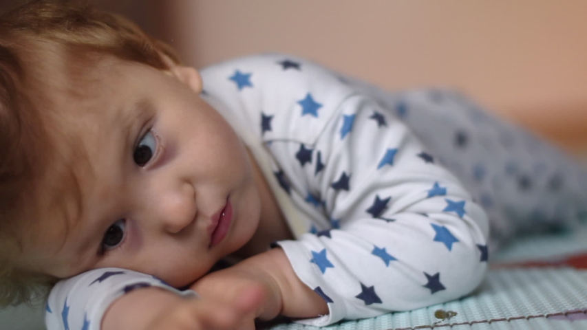 Portrait of a baby with cerebral palsy lying on his belly and playing at home. Special needs child. Handicapped baby boy close-up.