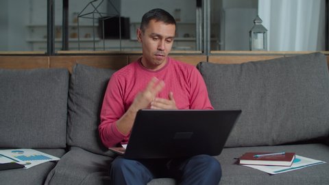 Deaf-mute male freelancer working on new business startup at home office, video conferencing online with partners on laptop pc talking using sign language, discussing financial charts and data.