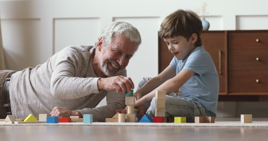 Happy old senior grandfather teach little grandson playing with wooden blocks on floor, carefree two generation family grandparent and cute small grandchild having fun building tower laughing at home Royalty-Free Stock Footage #1044003322