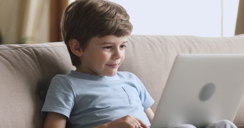 Curious preschool kid boy using laptop notebook browsing internet learning reading online social media content sit on sofa alone, cute little child obsessed with technology computer addiction concept