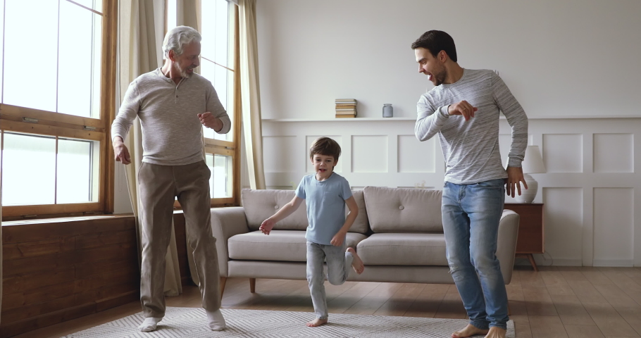 Cheerful joyful multi 3 three age generation men family having fun dancing jumping together in modern living room, cute little boy grandson, old grandpa and young dad funny leisure activity at home Royalty-Free Stock Footage #1044003412