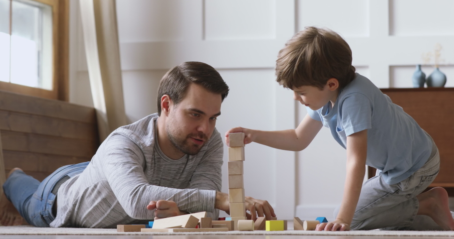 Happy adult parent dad helping cute preschool child son playing toys together on floor, caring father and little kid boy having fun laugh building constructor tower of colorful wooden blocks at home Royalty-Free Stock Footage #1044003427
