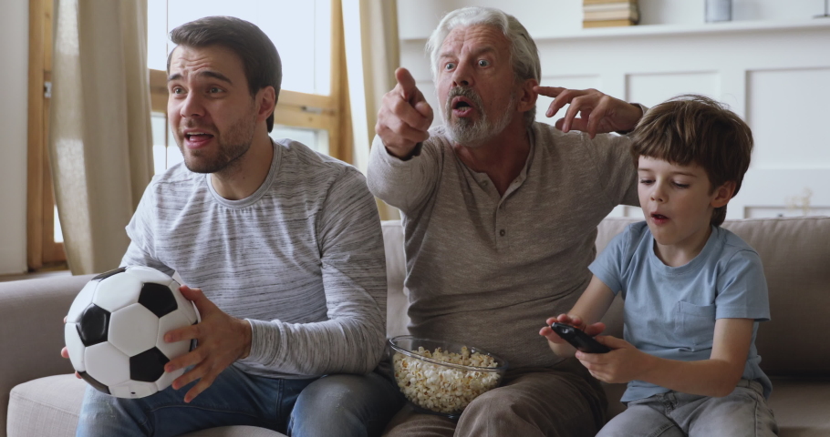 Frustrated disappointed three generations male family old grandpa, young son father and kid grandson fans supporters hold soccer ball watch tv sad by team losing football match sport game sit on sofa Royalty-Free Stock Footage #1044003445