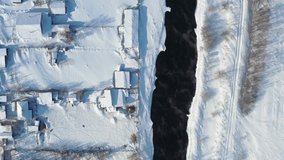 Aerial video view from lifting up and rotating drone on russian Altai country village Semiletka  in winter. Camera pointed down. River Koksha with banks covered by snow. Altai,  Siberia, Russia