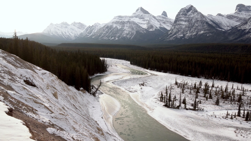 Nearly frozen river with tall jagged peaks in the background, Jasper National Park, Alberta Canada, Pan left shot