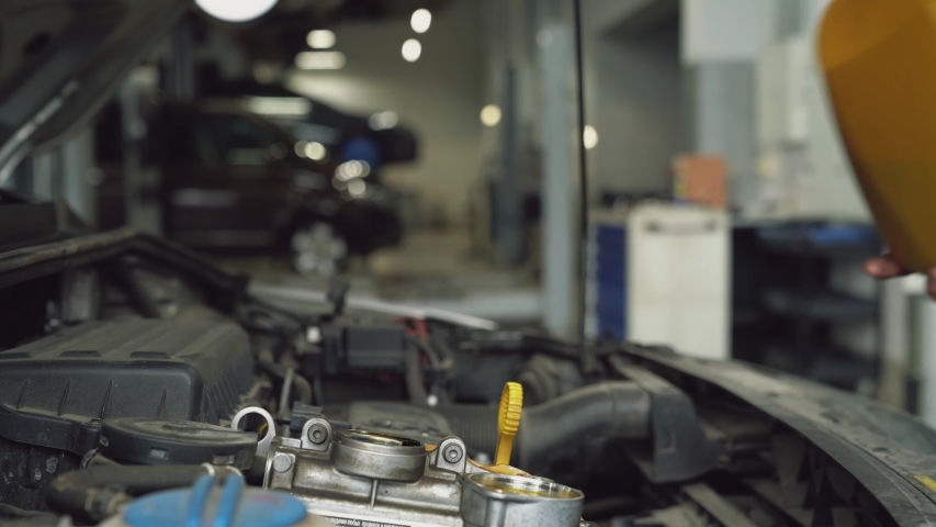 Close up of incognito car mechanic pouring oil into engine in motorway service station. Man working in opened bonnet and maintaining car in garage. Concept of car mechanics, work.