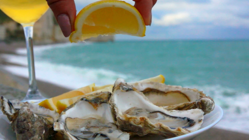 Lemon squeezed onto fresh oysters on the background of the ocean coast on a cloudy day in Etretat, France