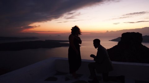 A man gives a ring to a woman proposing marriage Santorini. She surprises and becomes happy. Over the shoulder reference shot.man makes a marriage proposal to his girlfriend at sunset