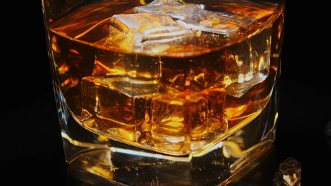 Golden whiskey in faceted glass with ice cubes rotating on black background macro. Alcoholic drinks, cocktail, alcohol.