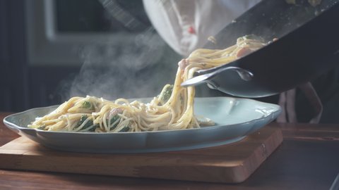 Chef puts finished spaghetti pasta from pan onto a plate in a restaurant kitchen. Food ingredient. Cooking on cuisine. Cooked for gourmet. Prepare food to eat. Gastronomy culinary. Delicious dinner.