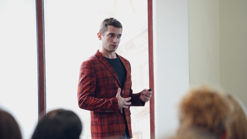 Young businessman conducts a meeting. Executive leader talking to the audience in the business forum. Manager make gestures while speaking.