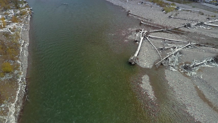 Aerial flying over the river bed of Middle Fork Flathead River. In the background is forest and mountains covered in snow. Glacier National Park, Montana, USA 