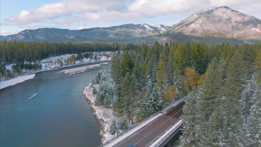 Aerial flying over Mountains and trees covered in snow, The Middle Fork Flathead River in West Glacier and a highway. Glacier National Park, Montana, USA 