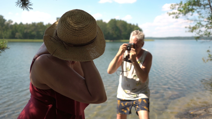 Elderly man taking picture of attractive senior woman with vintage camera on the beach. Funny active loving elderly couple carefree and happy together on vacation in Northern Europe, Finland