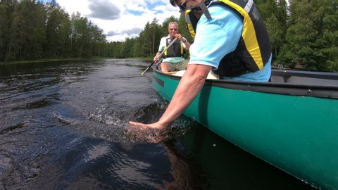 Mature couple canoeing on a forest lake in Finland. Woman splashing water on her husband. Active retirees enjoy outdoor sports. Sportive elderly people having fun at the nature.