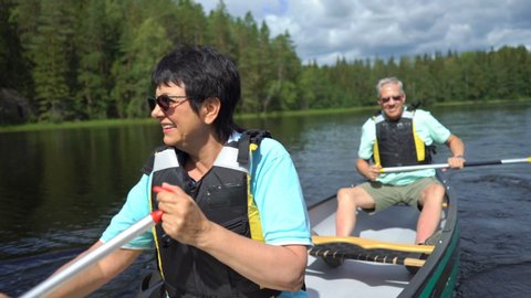 Mature couple canoeing on a forest lake in Finland. Active retirees enjoy outdoor sports. Sportive elderly people having fun at the nature.