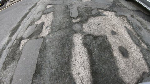 Vehicle driving over a damaged road which is covered in Potholes in the street. POV view from the van