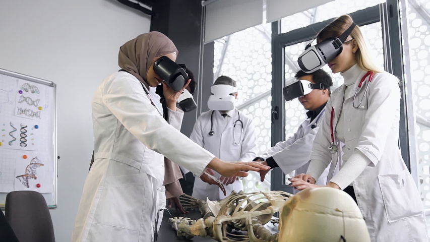 Attractive considerate multiethnic medical men and women wearing virtual reality headset and studing the structure of human skeleton