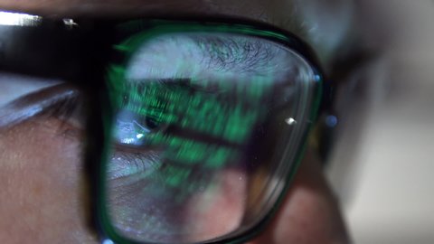 detail of a person’s eye looks, a hacker code is reflected on glasses