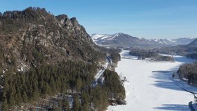 Aerial video view from drone flying over the winter forest road on the bank of river Katun. Altai mountains with pine snowbound taiga in winter season, Altai, Siberia, Russia.