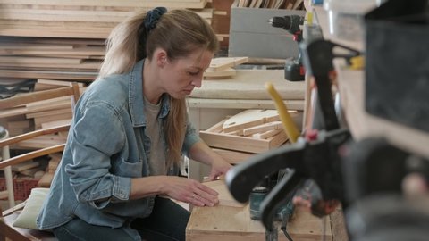 Joinery: a woman carpenter processes parts using a jigsaw, and sets aside. A woman is doing a man’s business: furniture manufacturing, craft workshop.