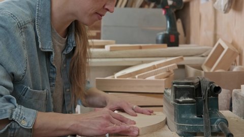 A woman does men's work: female carpenter works in a workshop and cuts wood using an electric jigsaw. Adult female craftsman makes wooden products.