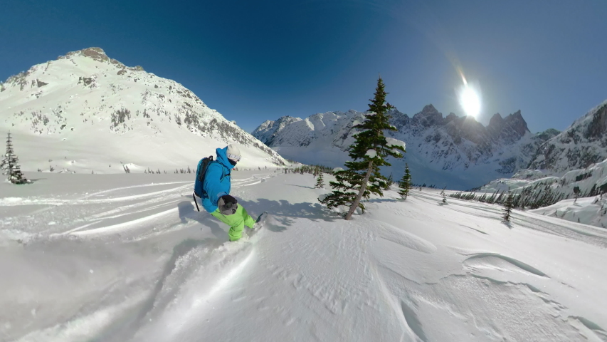 SELFIE: Awesome shot of mountains as man snowboards in the breathtaking Canadian backcountry. Extreme snowboarder shreds powder while carving between pine trees. Man heliboarding in British Columbia Royalty-Free Stock Footage #1044057841