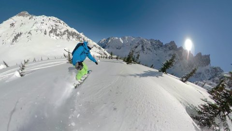 SELFIE: Awesome shot of mountains as man snowboards in the breathtaking Canadian backcountry. Extreme snowboarder shreds powder while carving between pine trees. Man heliboarding in British Columbia