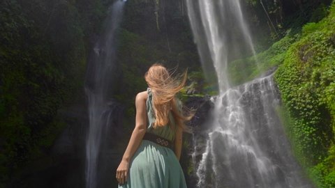 Young woman tourist visits the biggest waterfall on the Bali island - the Sekumpul waterfall. Slowmotion shot. Travel to Bali concept