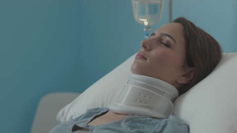 Injured woman lying in a hospital bed, she is wearing a cervical collar and getting IV therapy