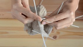 young womans hands knitting with gray metal needles and woolen thread on wooden table background, top view close-up full HD stock video footage in real-time