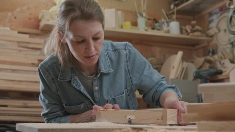 A woman is engaged in men's work and makes wooden furniture. Female carpenter processes parts and assembles a wooden product. The concept of a small craft business, a hobby.