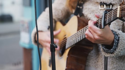 Close up of young woman busking playing acoustic guitar outdoors in street - shot in slow motion