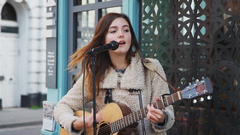 Young woman busking playing acoustic guitar and singing outdoors in street - shot in slow motion